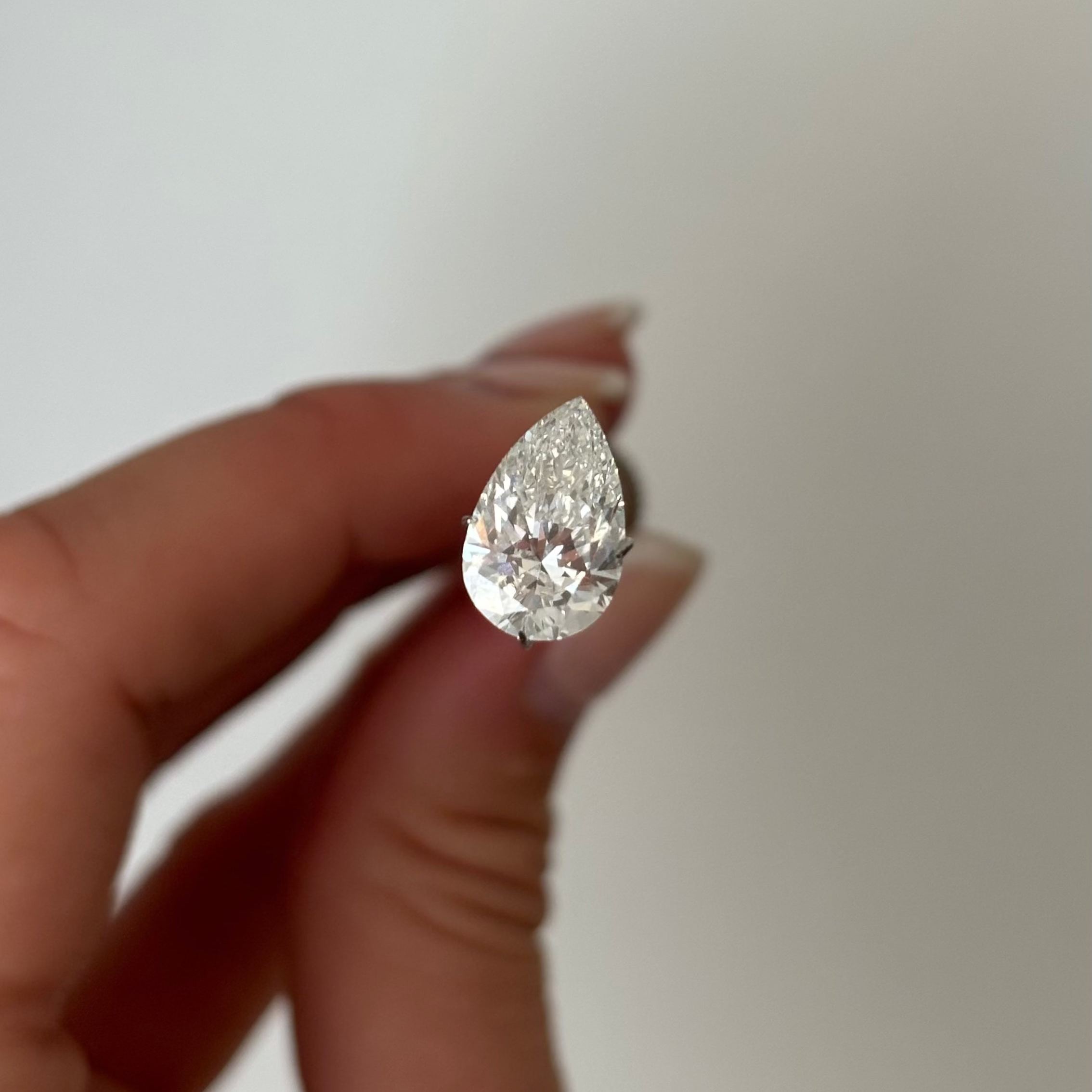 Teardrop-shaped diamond held between fingers against a neutral background